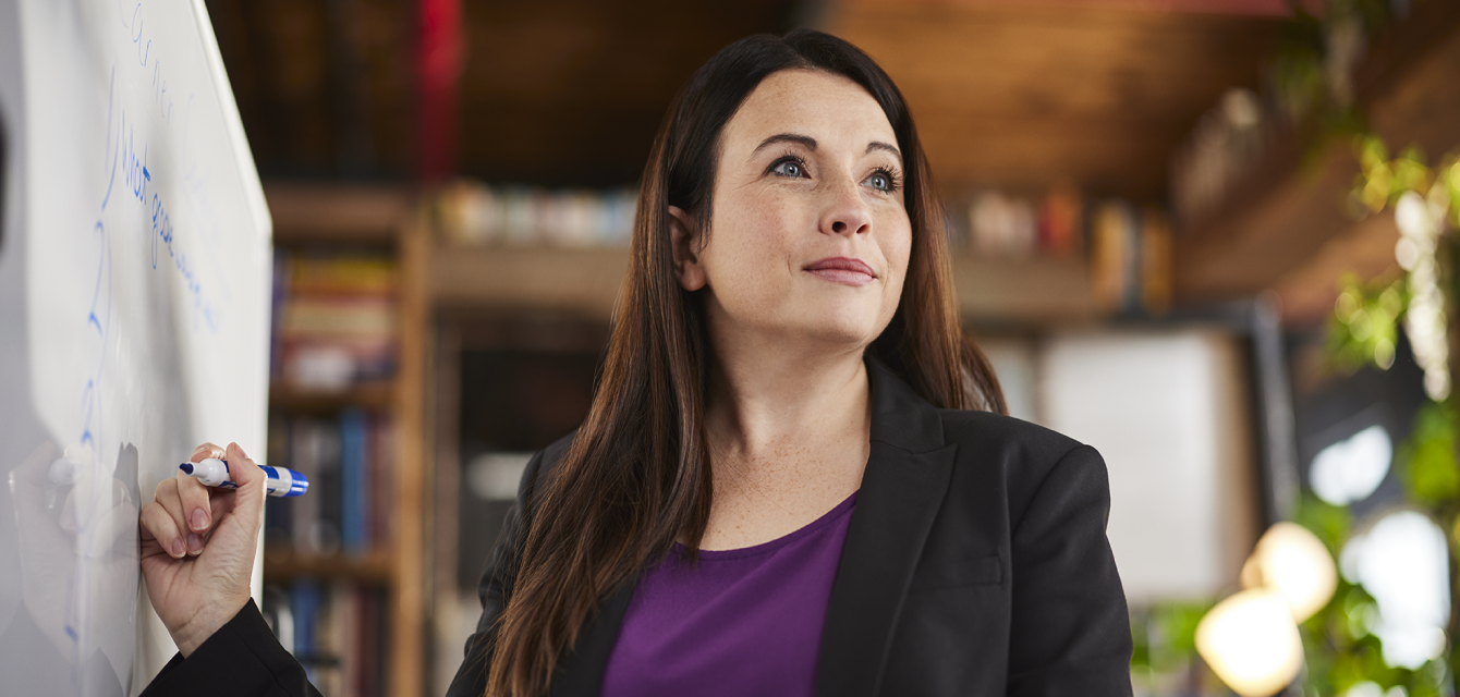 Woman in a blazer writing on a white board and looking into the distance