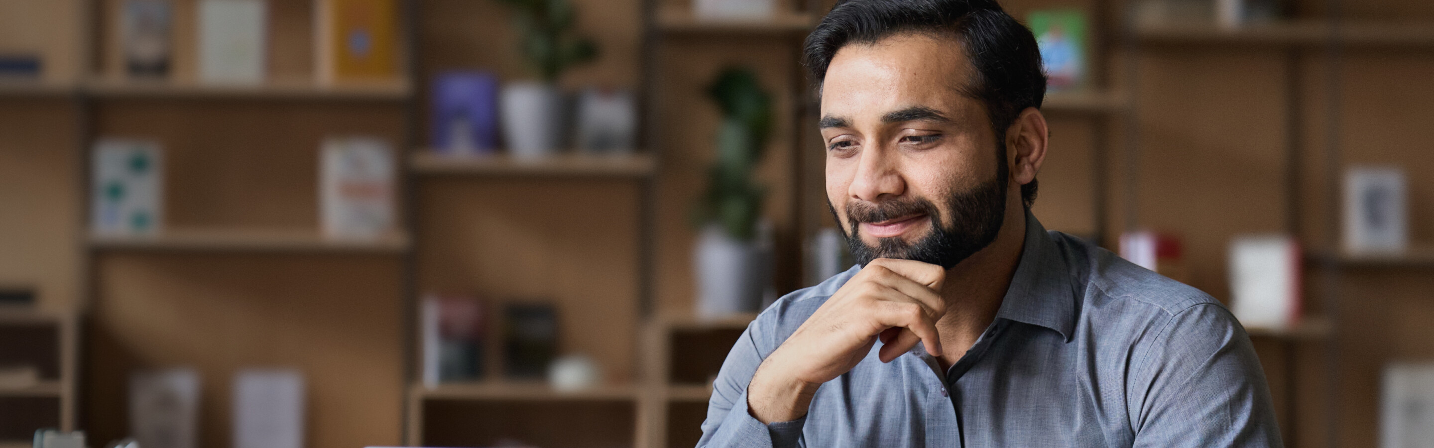 A man with a beard thinking while looking at a laptop