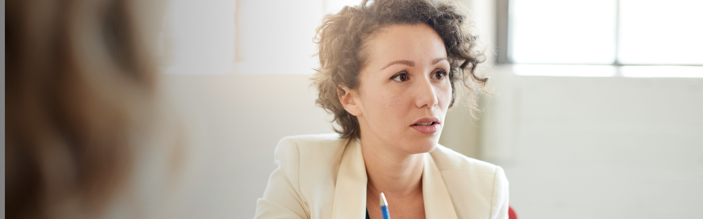 Woman in a blazer holding a pen and speaking to people outside the frame